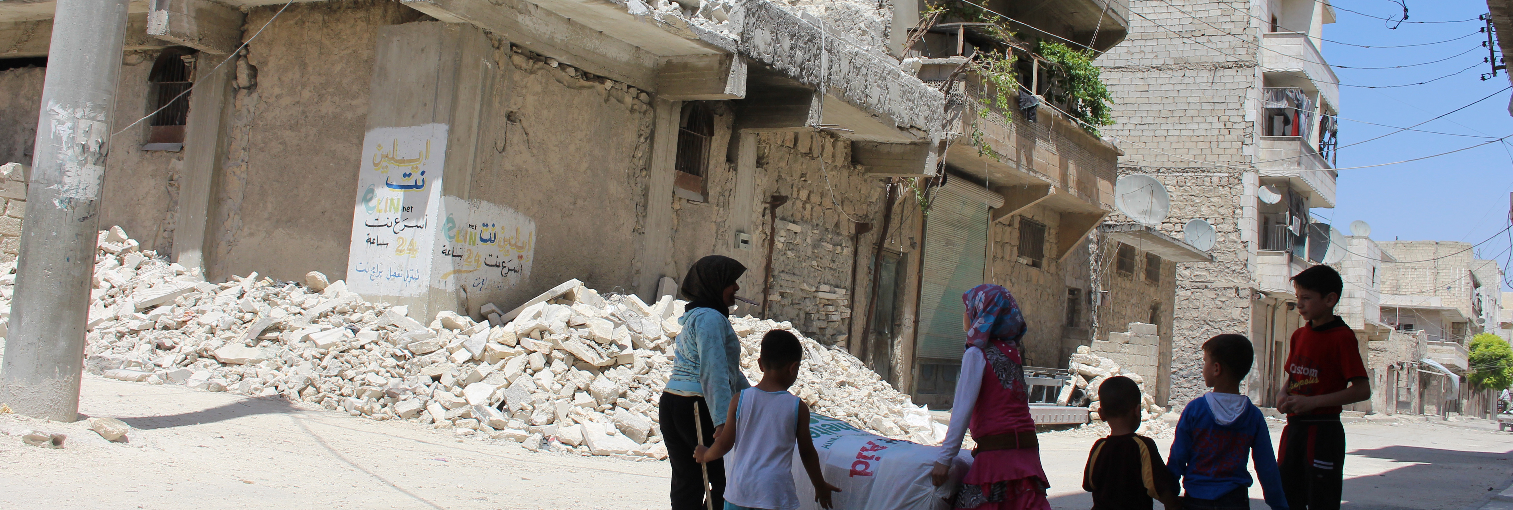 Kids play in street next to buildings damaged by bombing, Syria.