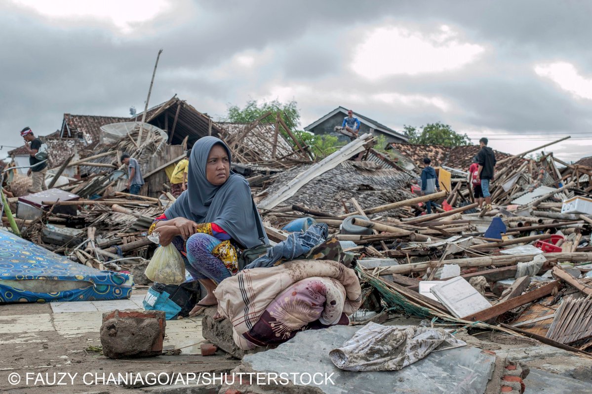 A tsunami survivor sits on a pice of debris as she salvages items from the location of her house in Sumur, Indonesia, . Doctors worked to save injured victims while hundreds of military and volunteers scoured debris-strewn beaches in search of survivors Monday after a deadly tsunami gushed ashore without warning on Indonesian islands on a busy holiday weekend.