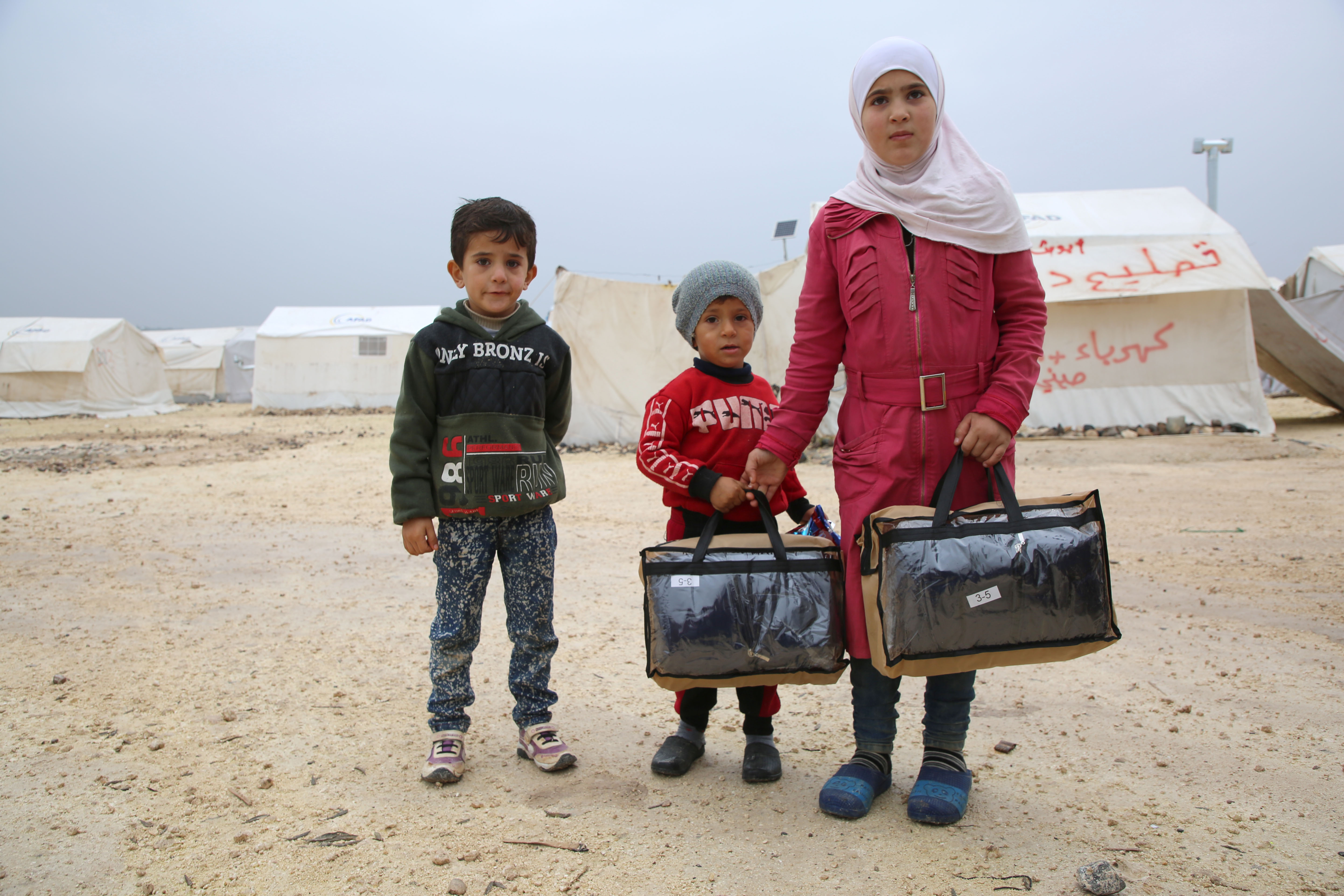 A girl and her young brothers in an encampment