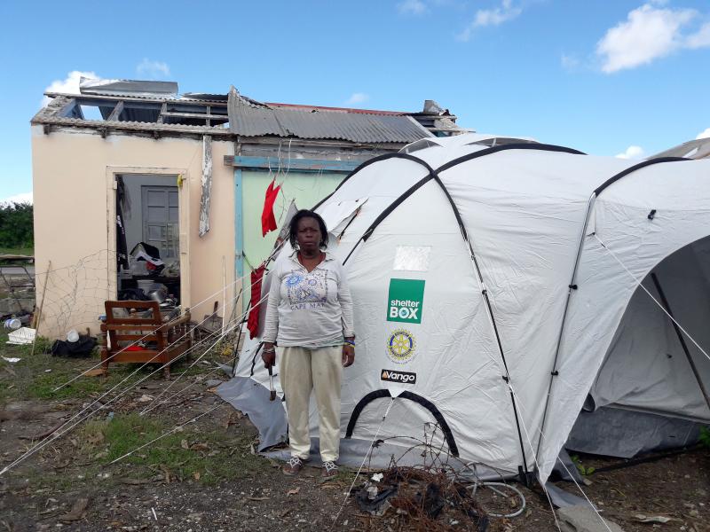 Amy with her tent tied down, next to a damaged building.