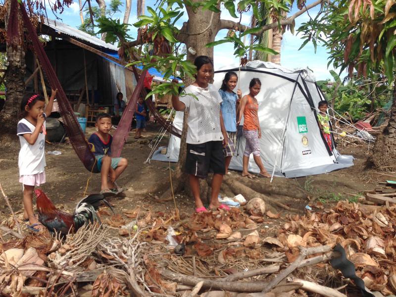 Kids relaxing in a jungle hammock with ShelterBox tent in rear