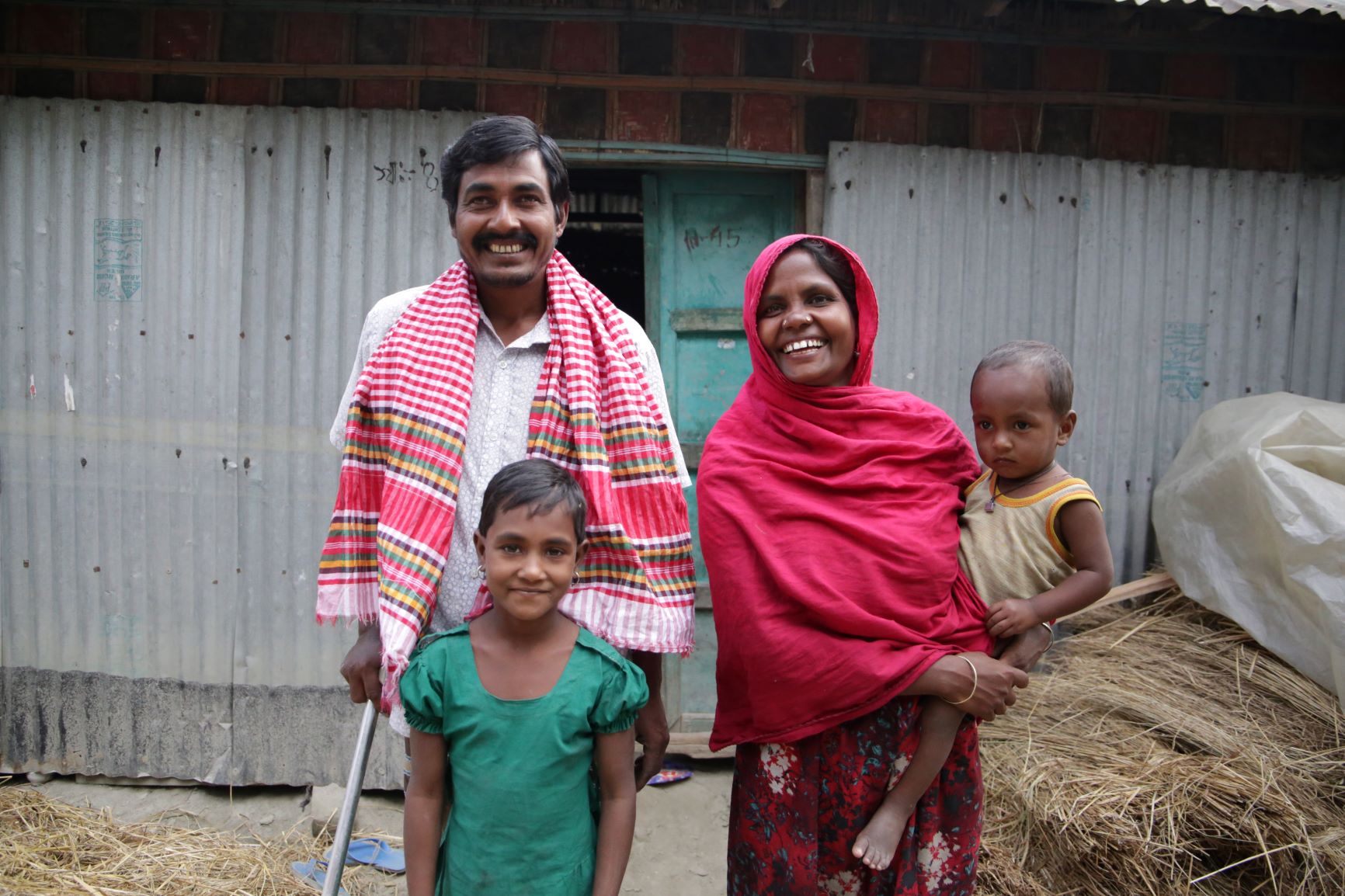 Behula, her husband, and 2 of their children outside their repaired home