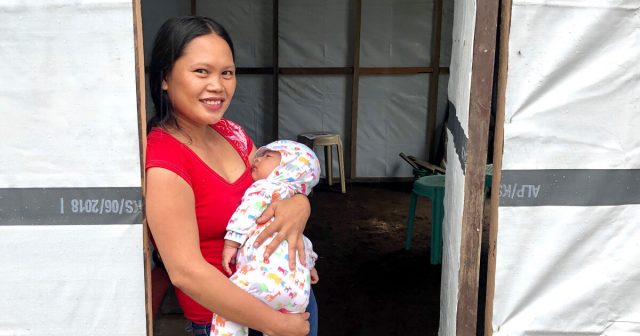 Young woman with infant daughter in home reinforced with tarpaulin
