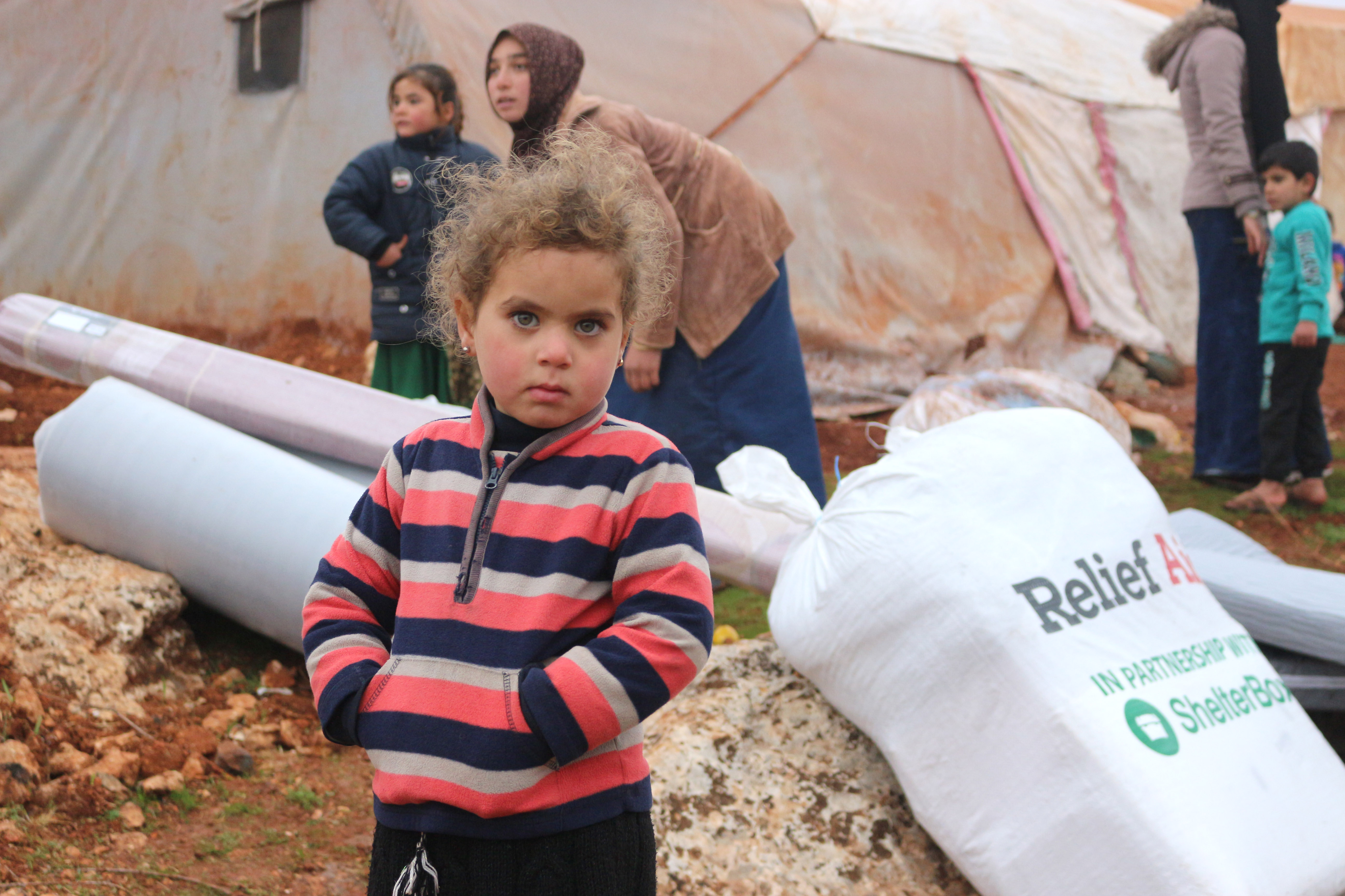 Child in front of aid items looking intently at camera