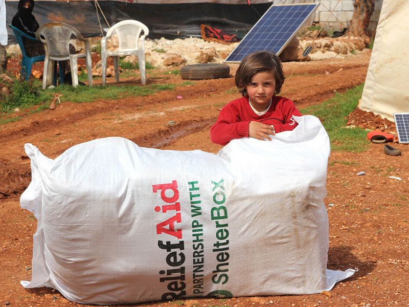 Child resting on large Relief Aid ShelterBox package, Syria 2020