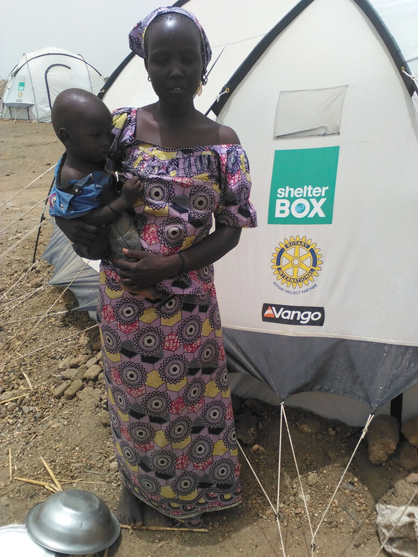 Modu carrying one of her young children outside her new tent