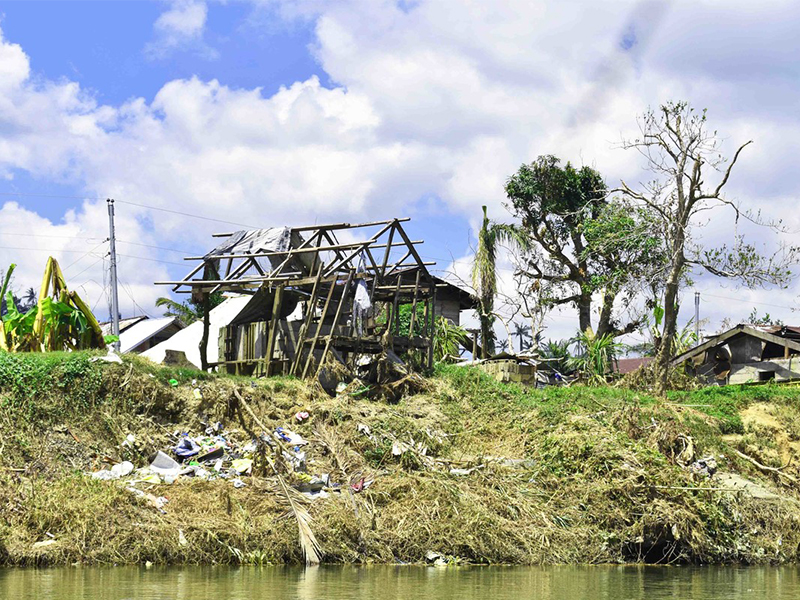 Debris scattered near a waterfront home, stripped of its roof and walls