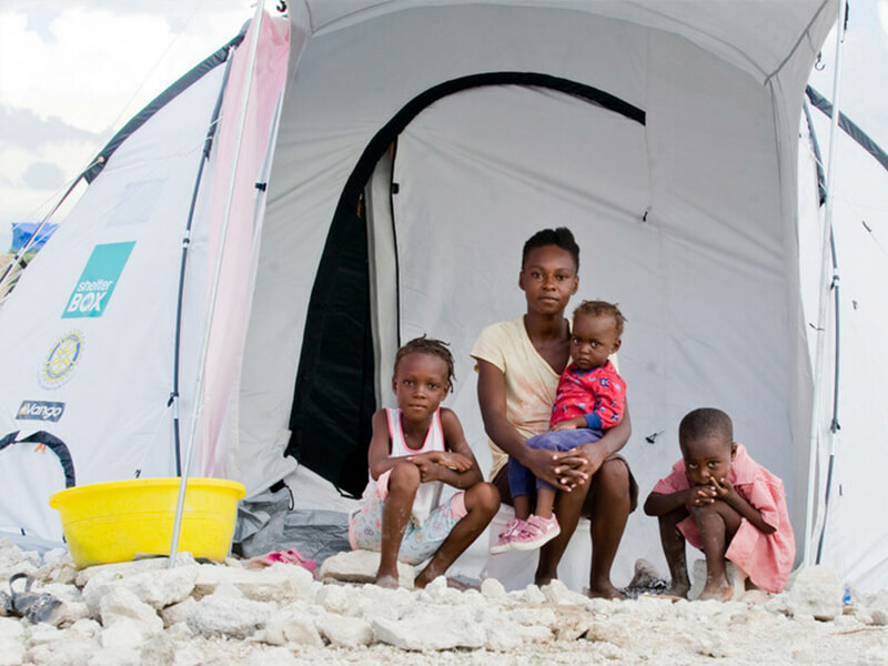 A family in Haiti sits outside of a ShelterBox tent they received