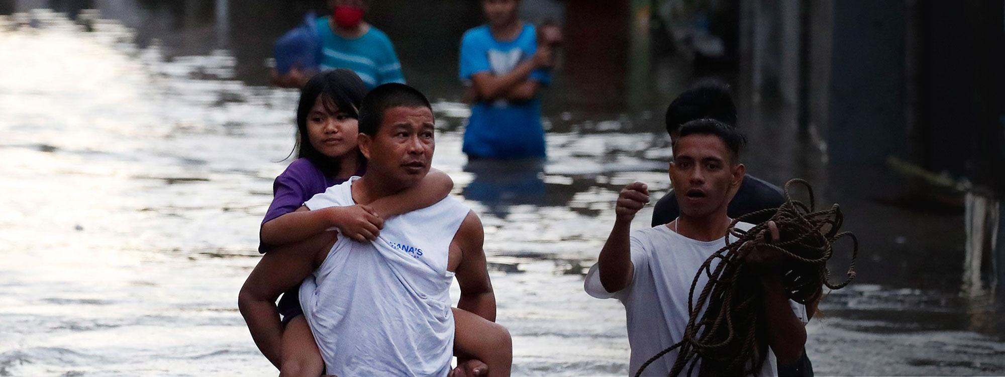 A man carries his daughter as he and others wade through waist deep water