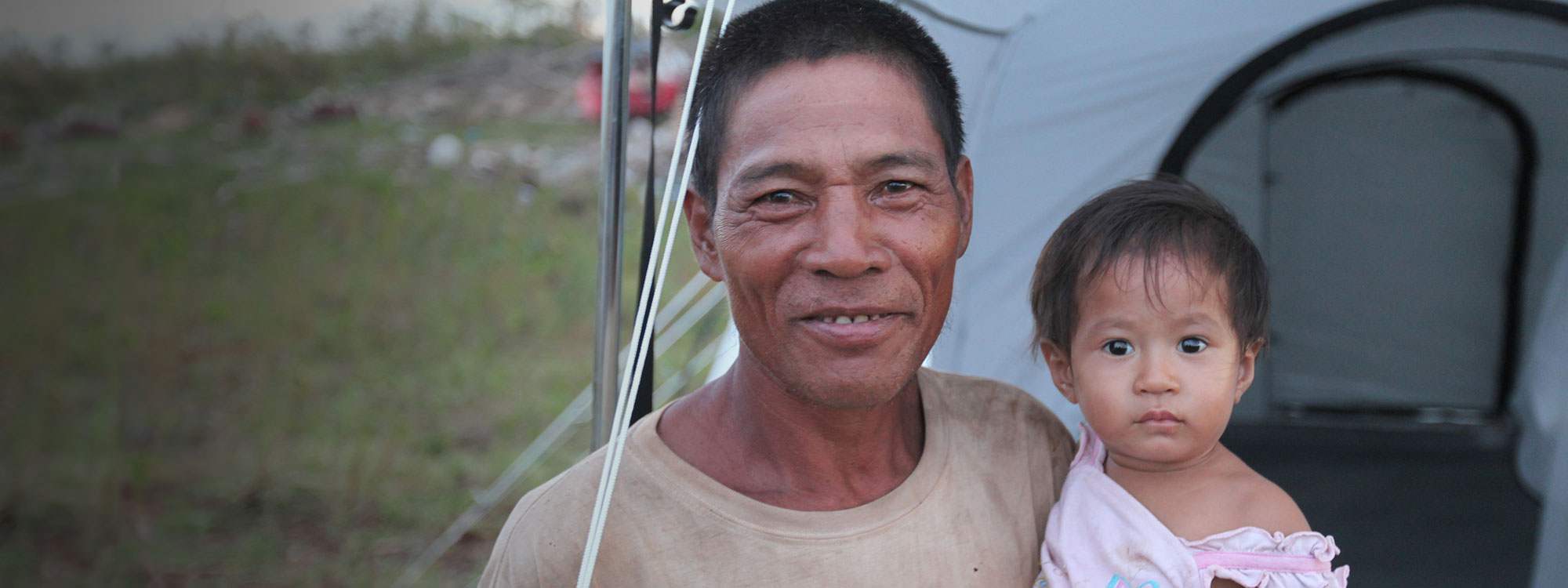 Filipino Man holding baby outside tent