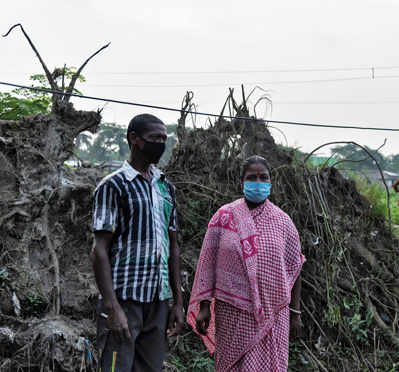 Phuleswari standing in front of mud, roots, and grass lifted up by the cyclone and flood waters